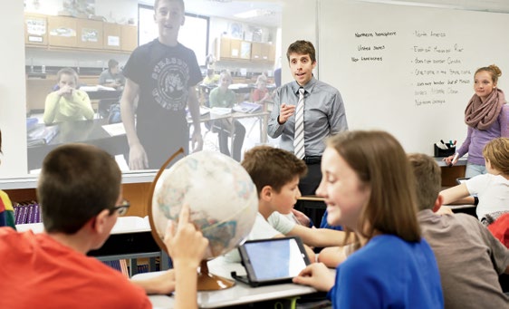 Photo de Joe Grabowski, enseignant agréé de l’Ontario, dans sa salle de classe. Il dirige une session de Skype avec ses élèves. À l’avant-plan, deux élèves pointent un pays sur le globe terrestre.