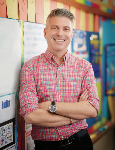 Photo de Michael Salvatori, chef de la direction et registraire, debout et souriant, appuyé contre le mur d’une salle de classe.