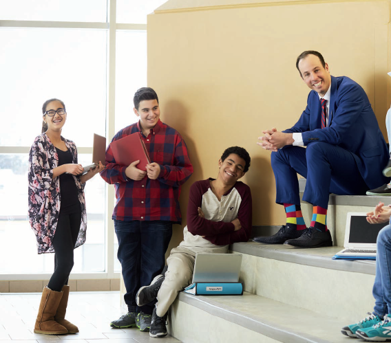Photo de Jason Dupuis, enseignant agréé de l’Ontario, assis sur des gradins. Cinq élèves, certains debout d’autres assis, sont avec lui. Ils rient tous.