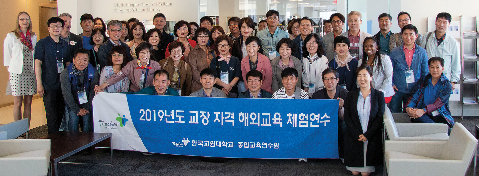 Photo d’un grand groupe de directions d’école coréennes souriant et tenant une bannière sur laquelle figure des caractères coréens.