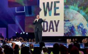 Photo de Martin Luther King III debout sur une scène, devant une grande enseigne «We Day». Il tient un microphone dans sa main droite pour s’adresser à la foule.