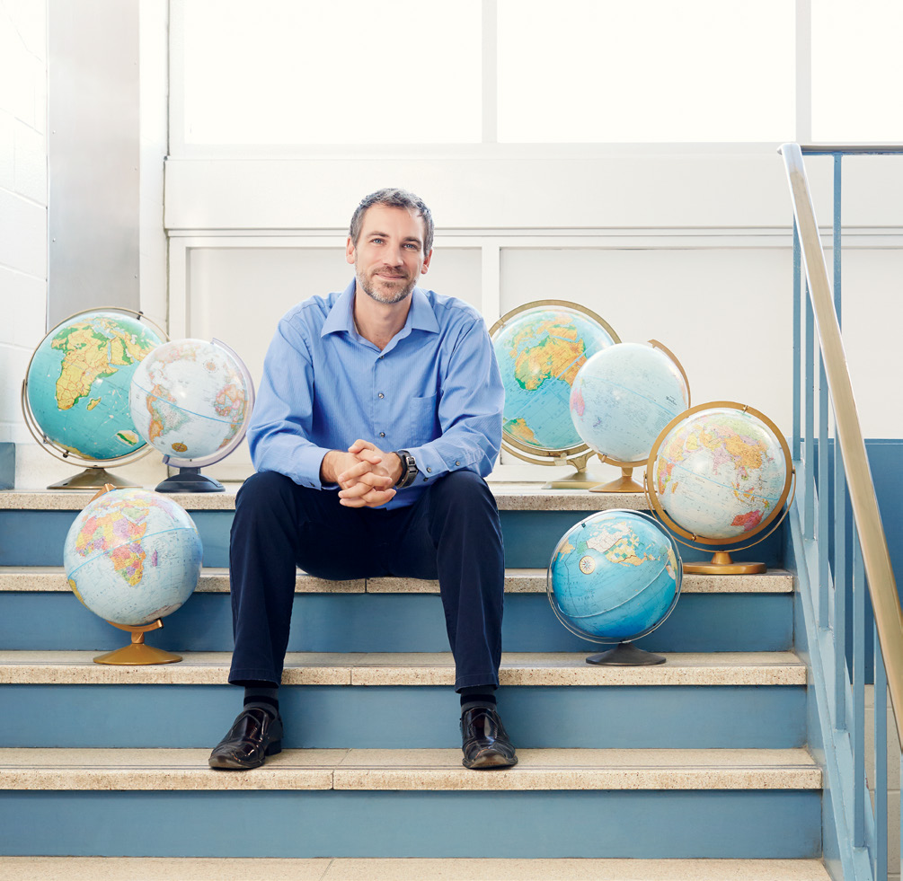 Photo de Brent Robillard, enseignant agréé de l’Ontario, assis sur un escalier. Il est entouré de globes terrestres.