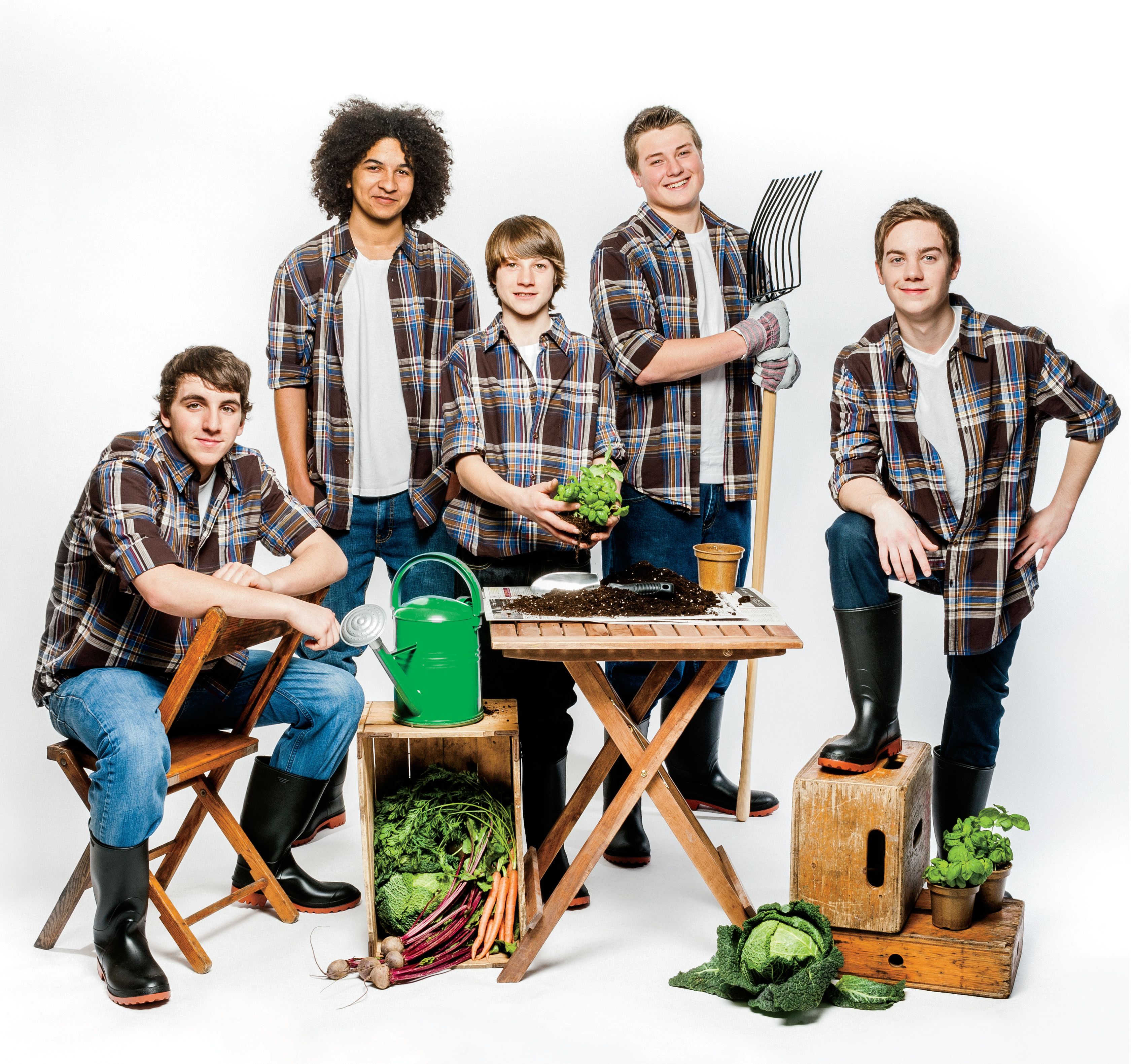 Photo de cinq adolescents qui tiennent des plantes ou des outils de jardinage. Un arrosoir, des légumes, une table et des boîtes en bois font partie de la scène.