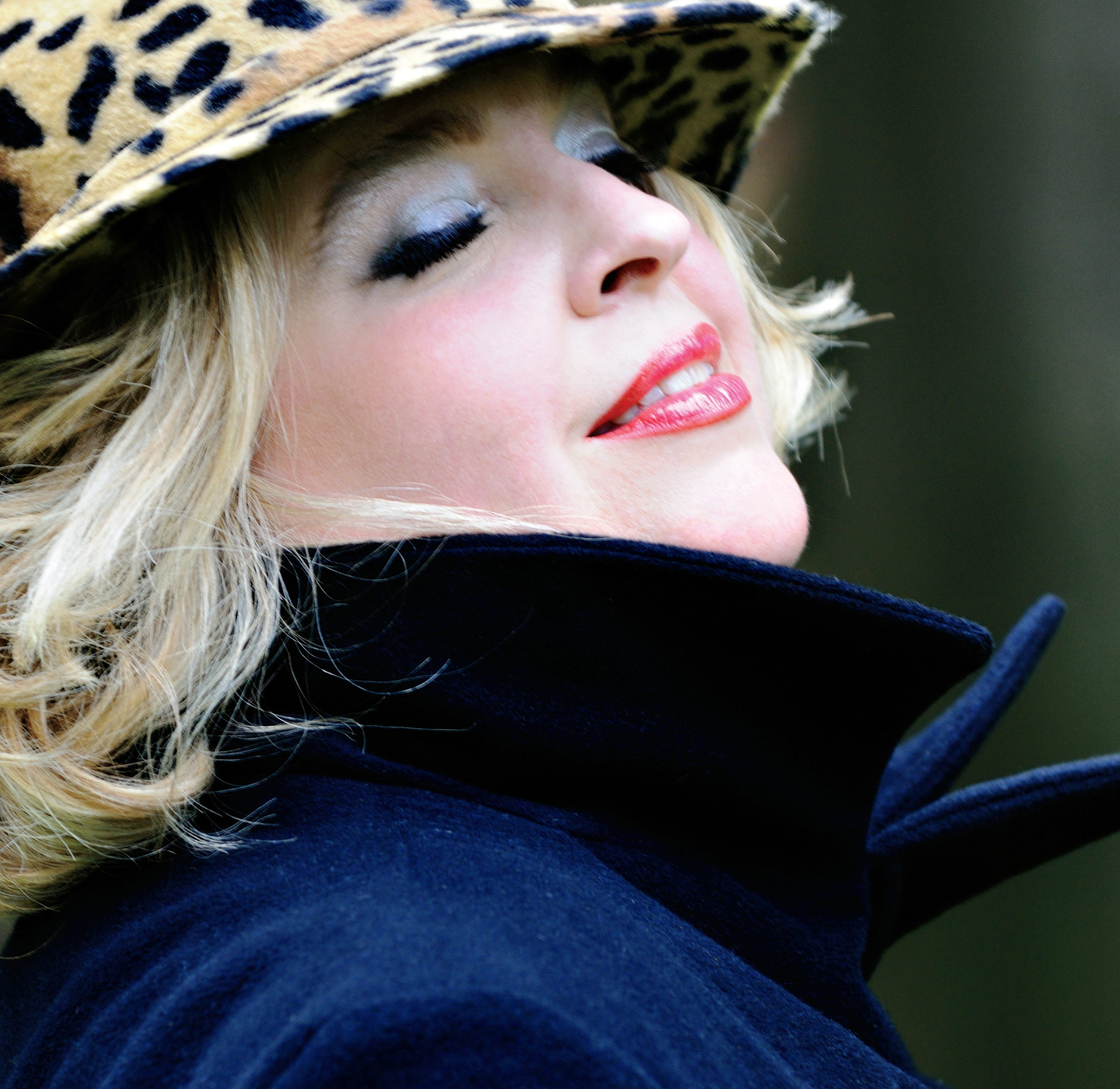 Photo en gros plan de Karina Gauvin, soprano, le sourire aux lèvres. Elle porte un chapeau en léopard et a relevé le col de son manteau. Elle a les yeux fermés et la tête rejetée en arrière.
