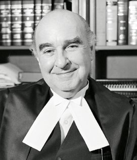 Photo en noir et blanc du juge Sydney Lewis Robins O. ONT., QC., devant des étagères de livres.