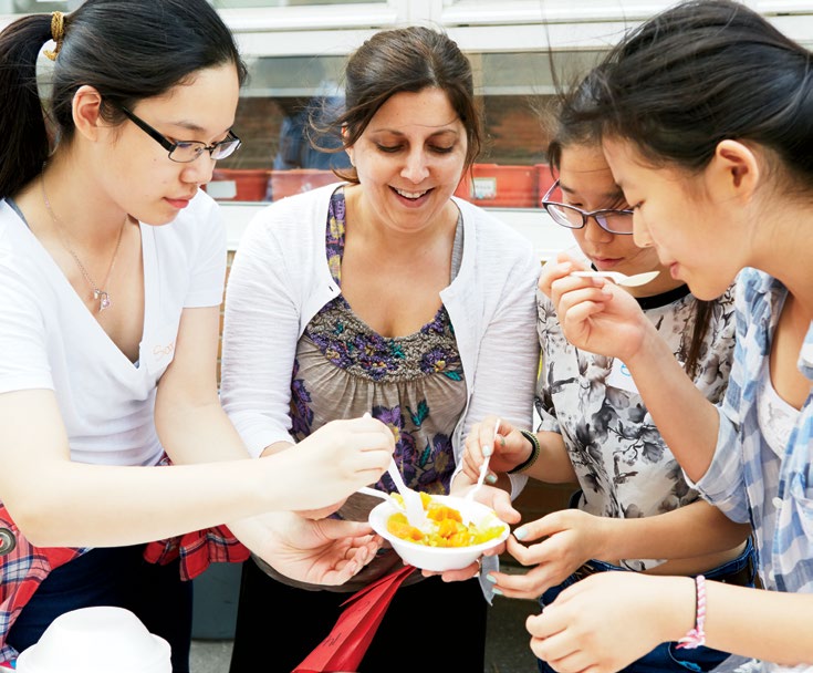 Photo d’une enseignante entourée de trois élèves. Ils goûtent un nouveau plat.