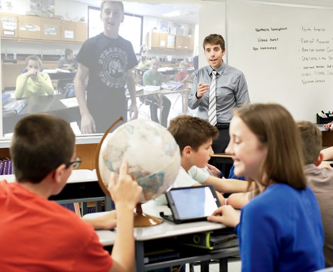 Photo de Joe Grabowski, enseignant agréé de l’Ontario, dans sa salle de classe. Il dirige une session de Skype avec ses élèves. À l’avant-plan, deux élèves pointent un pays sur le globe terrestre.