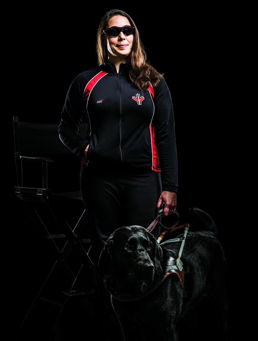 Photo de Victoria Nolan, enseignante agréée de l’Ontario, sur fond noir. Elle porte des verres fumés. Dans la main gauche, elle tient la laisse de son chien-guide (un labrador noir).