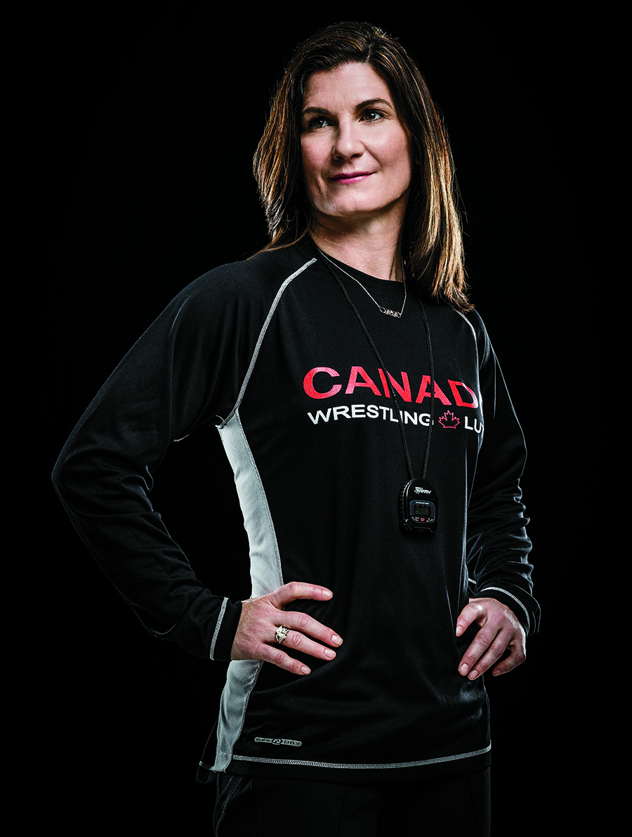 Photo de Tonya Verbeek, enseignante agréée de l’Ontario, sur fond noir. Elle a les mains sur les hanches. Elle porte le chandail de l’équipe de lutte du Canada aux Jeux panaméricains de 2015 à Toronto.