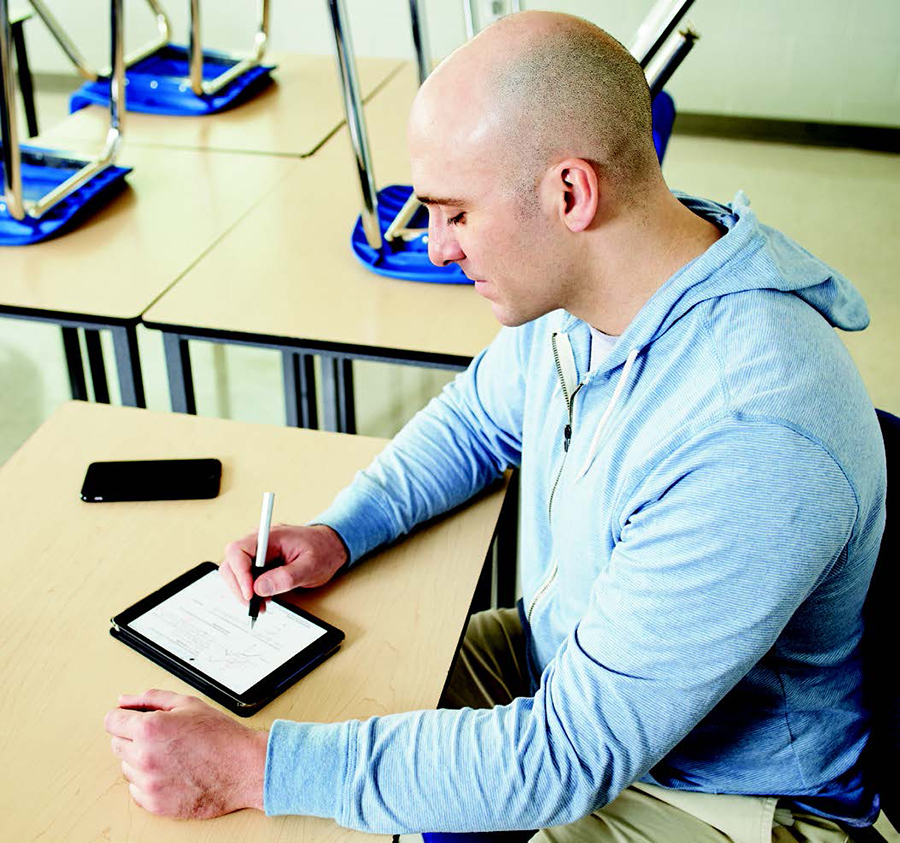 Photo de Jacopo Stifani, assis à une table dans une salle de classe vide. Il utilise sa tablette à l’aide d’un stylet.