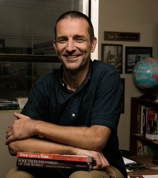 Photo de Brad Woods, enseignant agréé de l’Ontario, assis, appuyé sur des livres qui sont sur ses genoux.