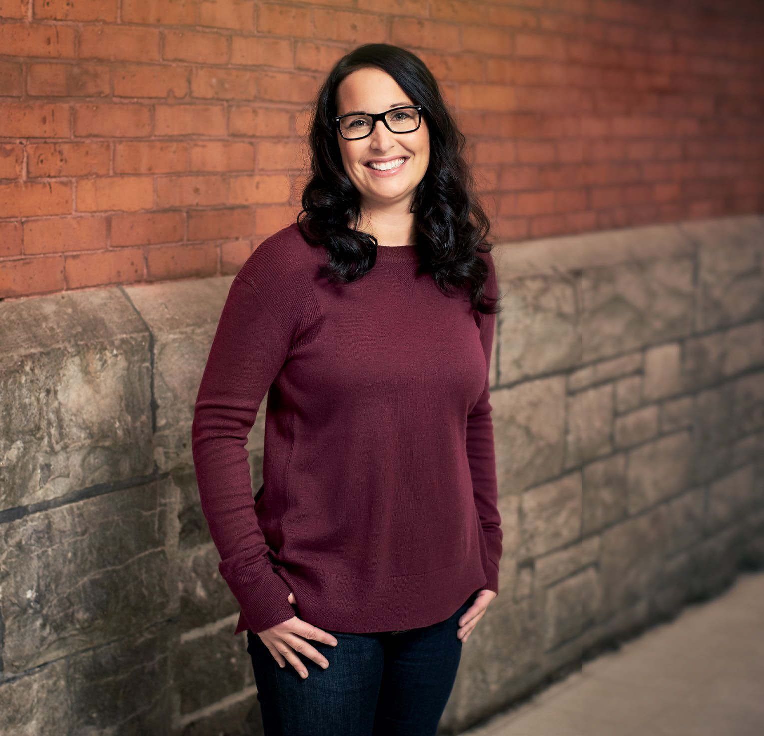 Photo de Chantal Larivière, enseignante agréée de l’Ontario, debout, les pouces dans les poches de son pantalon devant un mur de briques et de pierres.