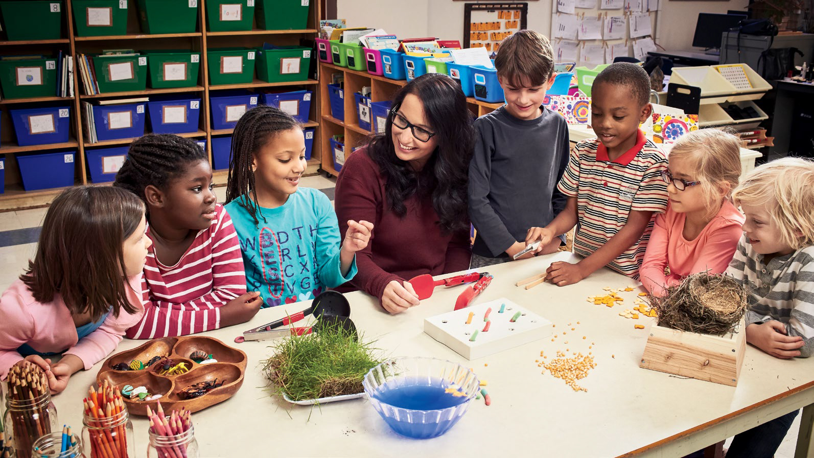 Photo de Chantal Larivière, enseignante agréée de l’Ontario, assise à une table avec de jeunes élèves. Elle regarde une élève qui tente de faire claquer ses doigts.