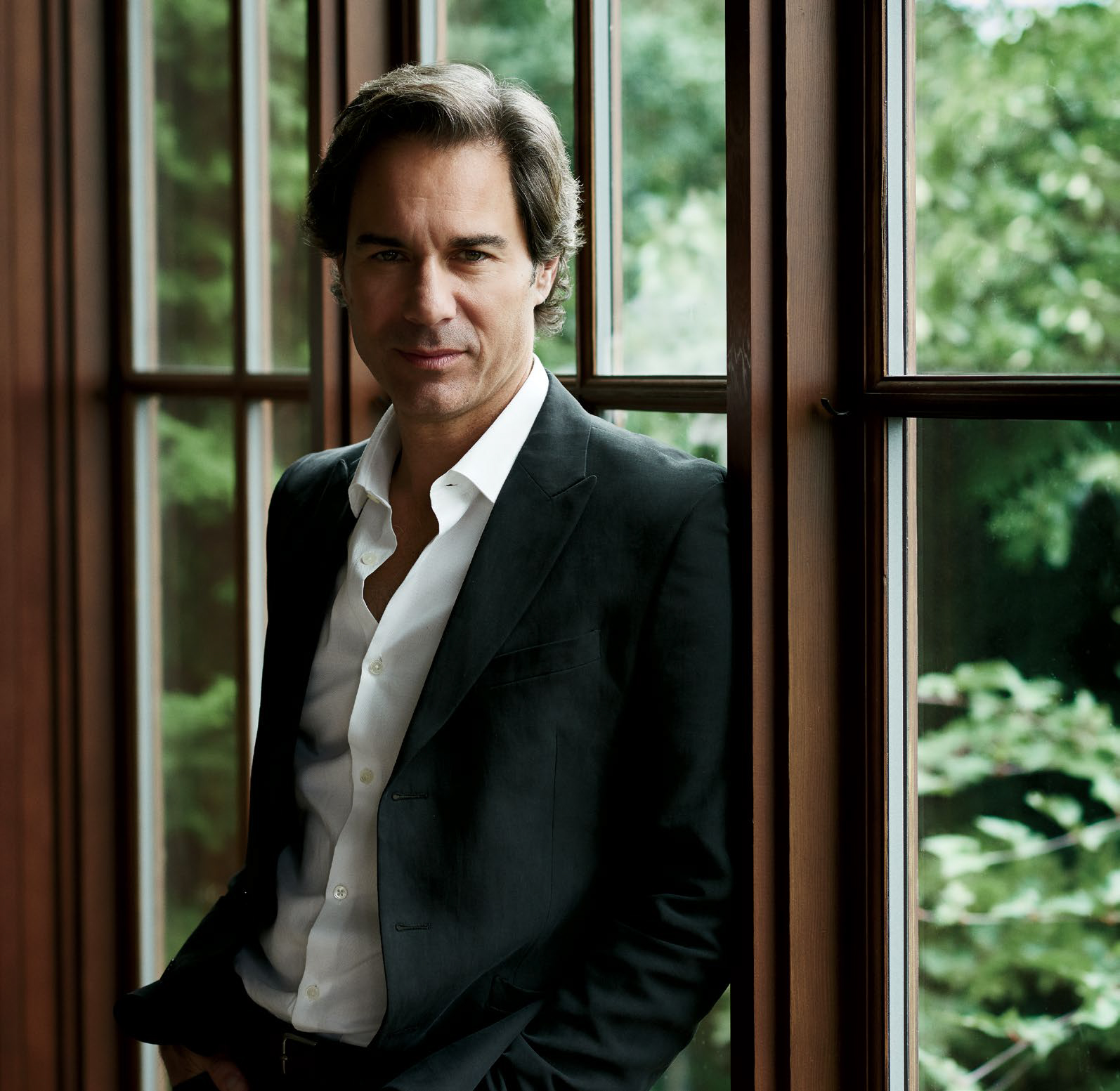 Photo de l’acteur Eric McCormack, debout devant une fenêtre, appuyé contre l’embrasure d’une porte.