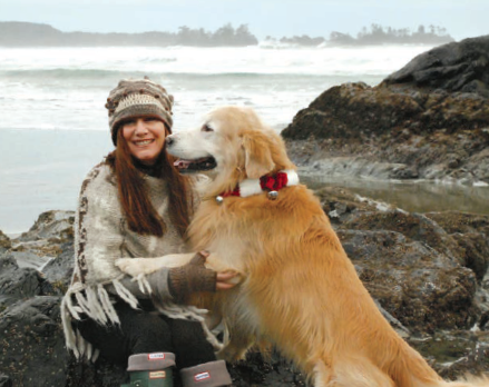 Photo de Suzi Beber, ancienne enseignante de Kirstine Stewart à l’Acton High School avec un chien de race golden retriever. Elle est assise sur des rochers du rivage de Tofino, C.-B.