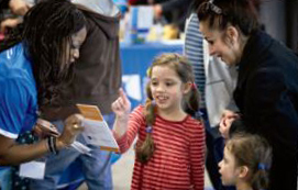 Photo d’un membre du personnel de l’Ordre. Elle montre un livret à deux jeunes enfants et à une mère à l’occasion de l’Ottawa Parent & Child Expo.