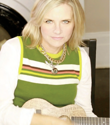 Photo de la chansonnière Melanie Doane. Elle tient une guitare et fixe l’objectif d’un regard intense.