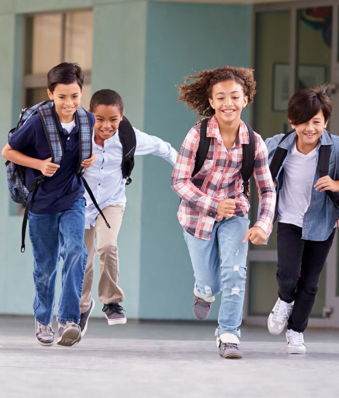 Photo d'un groupe de quatre jeunes élèves souriant qui courent ensemble avec leur sac à dos.