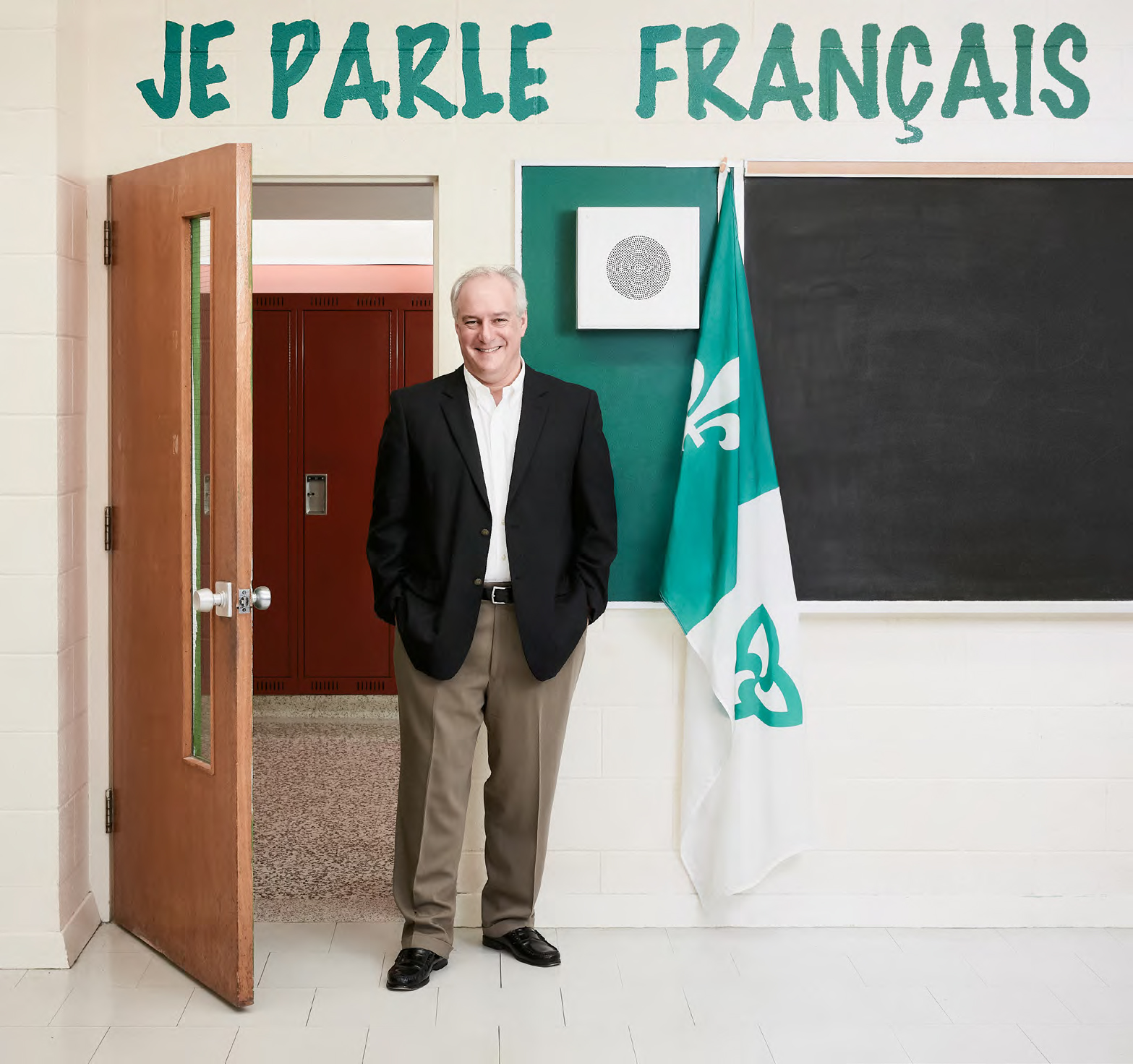 Pierre Riopel, enseignant agréé de l'Ontario, debout dans une salle classe, à côté d'un drapeau orné de la fleur de lys et de la trille 