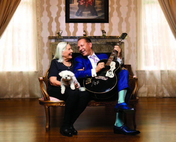 Photo de Michael Wekerle, entrepreneur et vedette de l'émission télévisée Dragon's Den, assis sur une chaise avec sa mère, Hermine. Ils se regardent et sourient. M. Wekerle tient une guitare dans ses mains et sa mère a un chien sur les genoux.