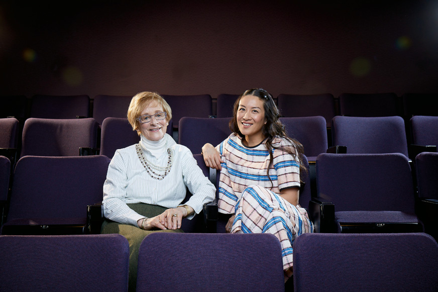 Photo d’Elaine «Lainey» Lui assise en compagnie de son enseignante Caryl Grimsley dans les fauteuils d’un théâtre.
