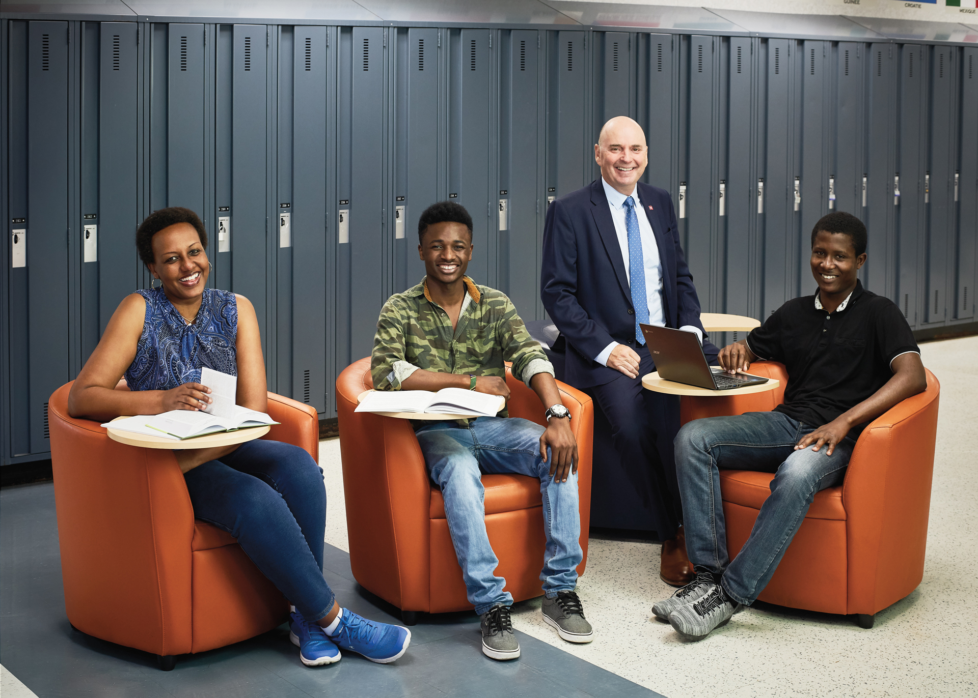 Photo de Jean-Pierre Dufour, enseignant agréé de l'Ontario, souriant, et de trois élèves souriants, assis sur des fauteuils dans un espace pour étudiants de l'école.