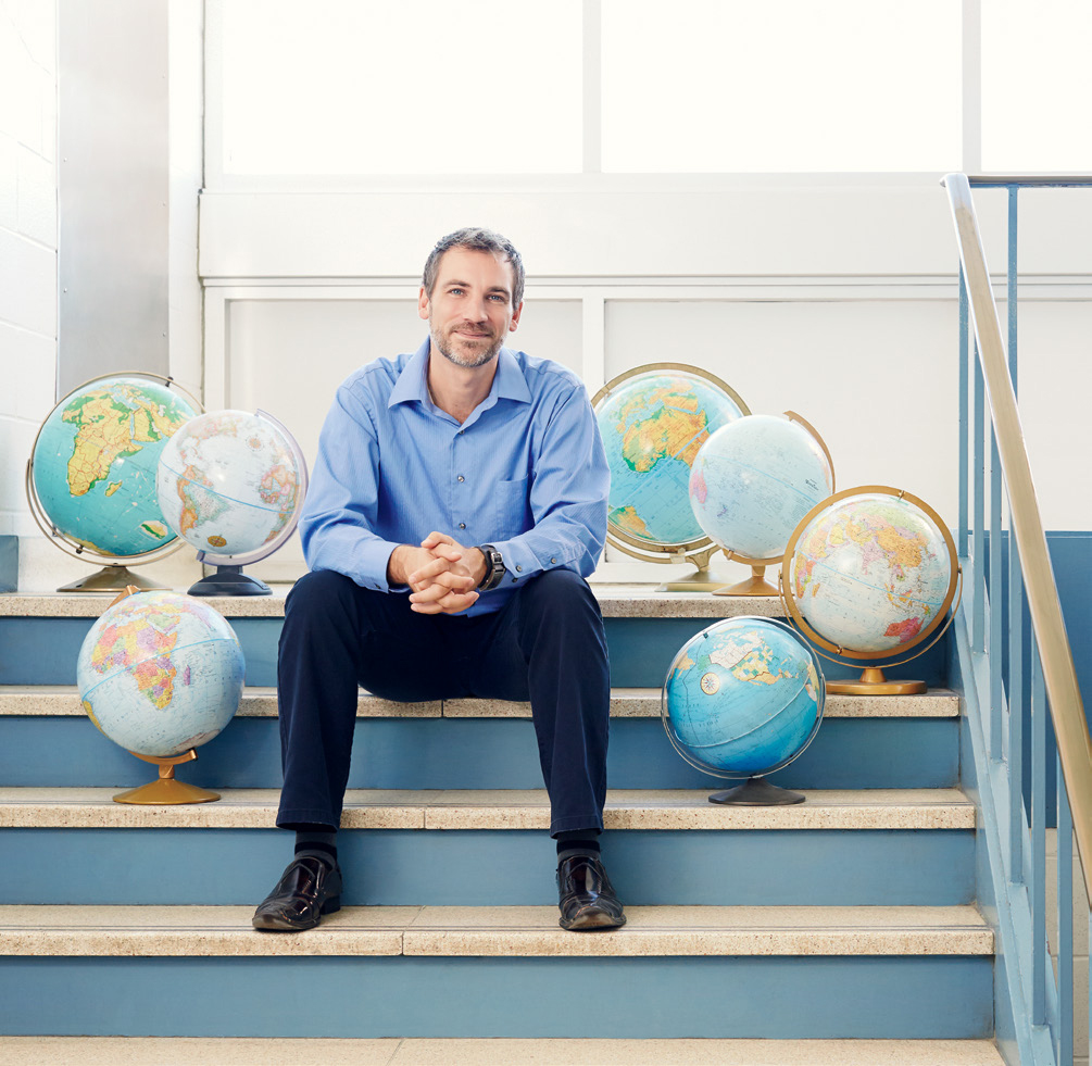 A photo of Brent Robillard seated on some stairs surrounded by globes.