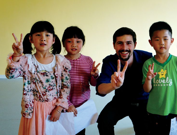 A photo of Josh Rose standing with three students. They are all making the peace sign with their fingers.