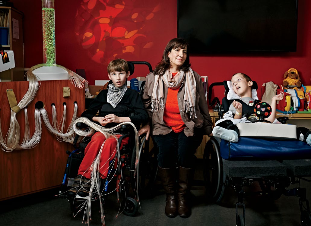 A photo of Renee Hiltz sitting in a hospital room. Renee is flanked by two young students in wheelchairs.