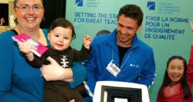 Photo of Julia Lazarito with 10-month-old baby Dominic. Dominic is holding a book received from a staff member at the College booth at the London Baby Expo.