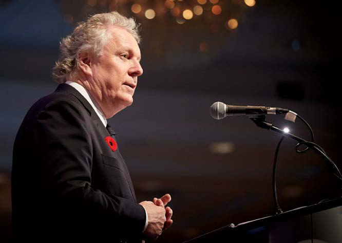 Photo of Jean Charest speaking into a microphone at the College's ''2014 Inspiring Public Confidence'' conference. Jean is wearing a Remembrance Day poppy.
