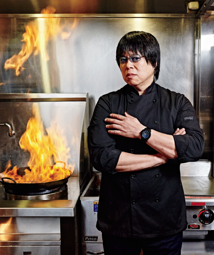 Photo of MasterChef Canada’s Alvin Leung. Alvin is standing in a kitchen and has an intense look. Behind Alvin is a wok with flames.