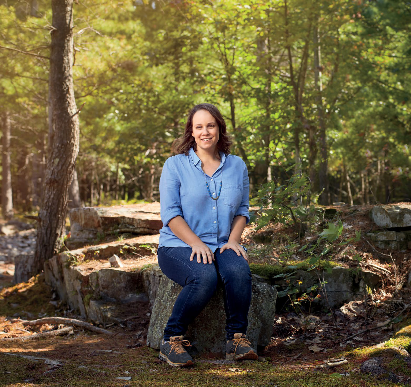 A photo of Petra Eperjesi, Ontario Certified Teacher sitting on a tree stump.