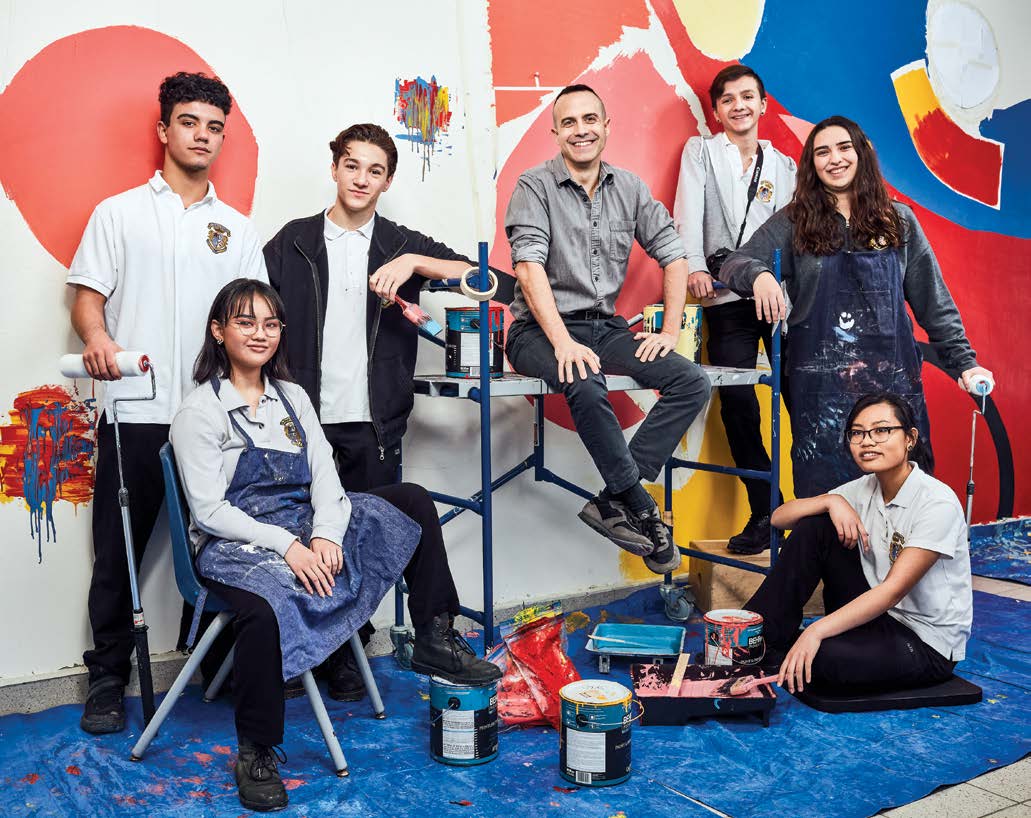 Photo of John Senisi, Ontario Certified Teacher seated on a paint scaffold surrounded by students.