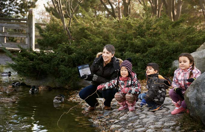 A photo of Laurel Fynes, Ontario Certified Teacher, crouching near a stream with three young students.