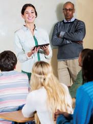 Image of a teacher standing at the front of a class and holding a tablet.