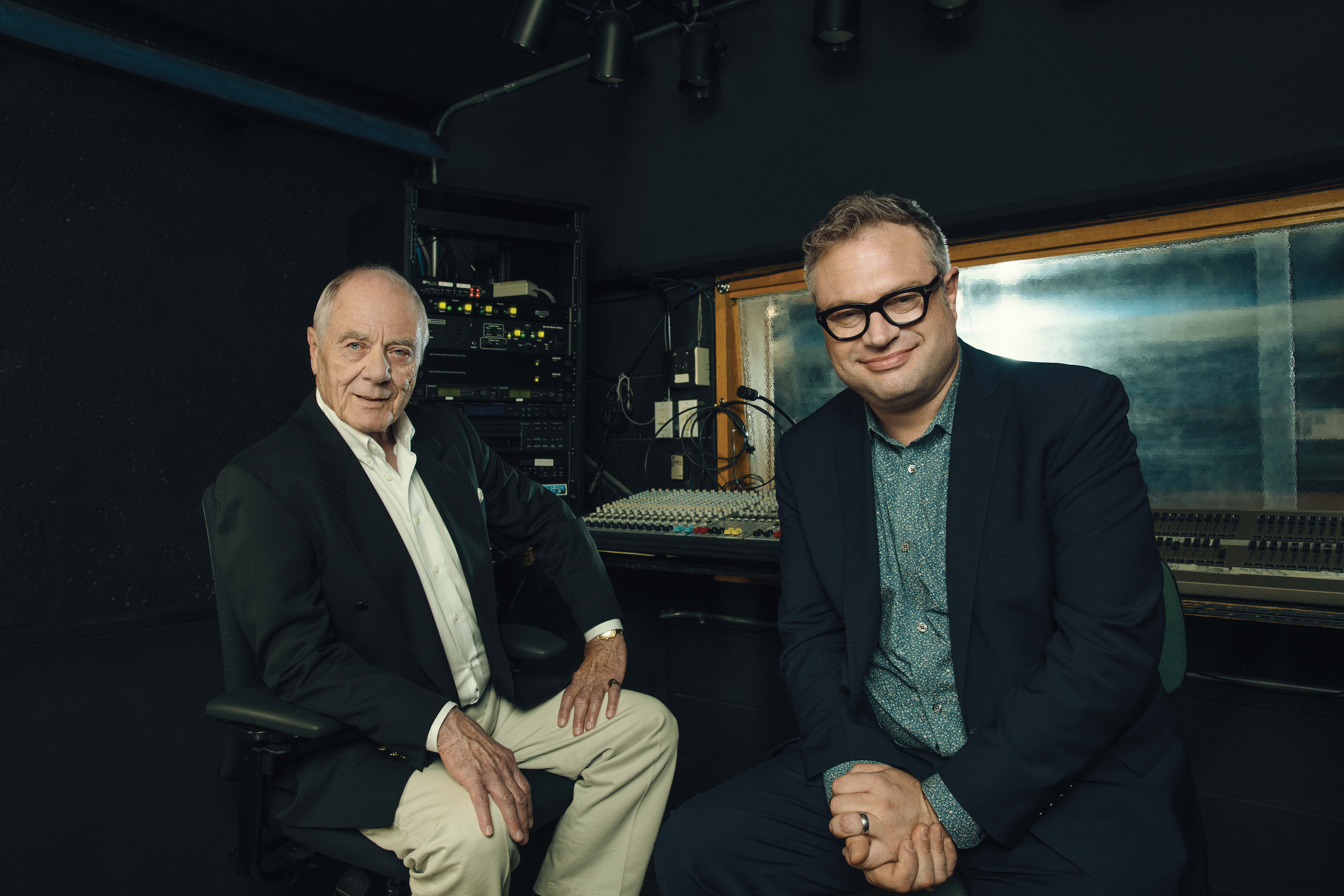Photo of singer-songwriter Steven Page sitting beside his former choir conductor, Garth Allen in a music studio.
