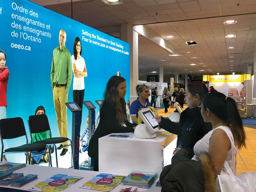 Photo of College representatives at a booth, speaking to members of the public.