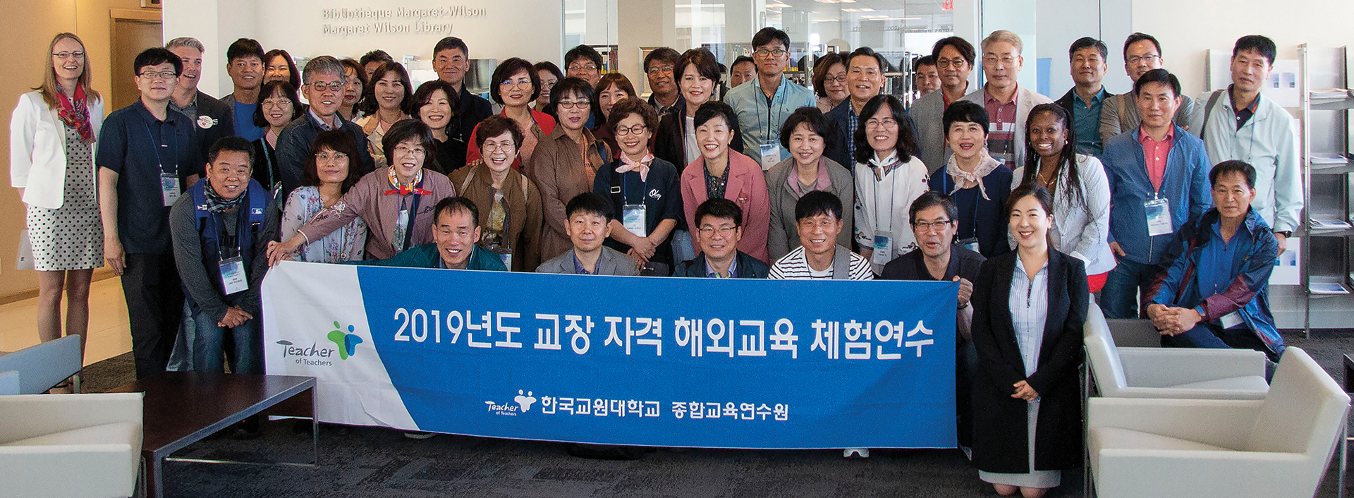 Photo of a large group of South Korean principals smiling and holding a banner with Korean characters on it. 