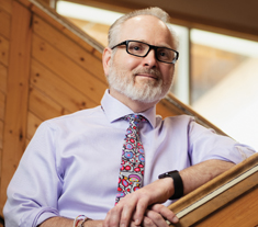 Photo of Chris Mara, Ontario Certified Teacher, smiling while resting arms along a wooden banister.
