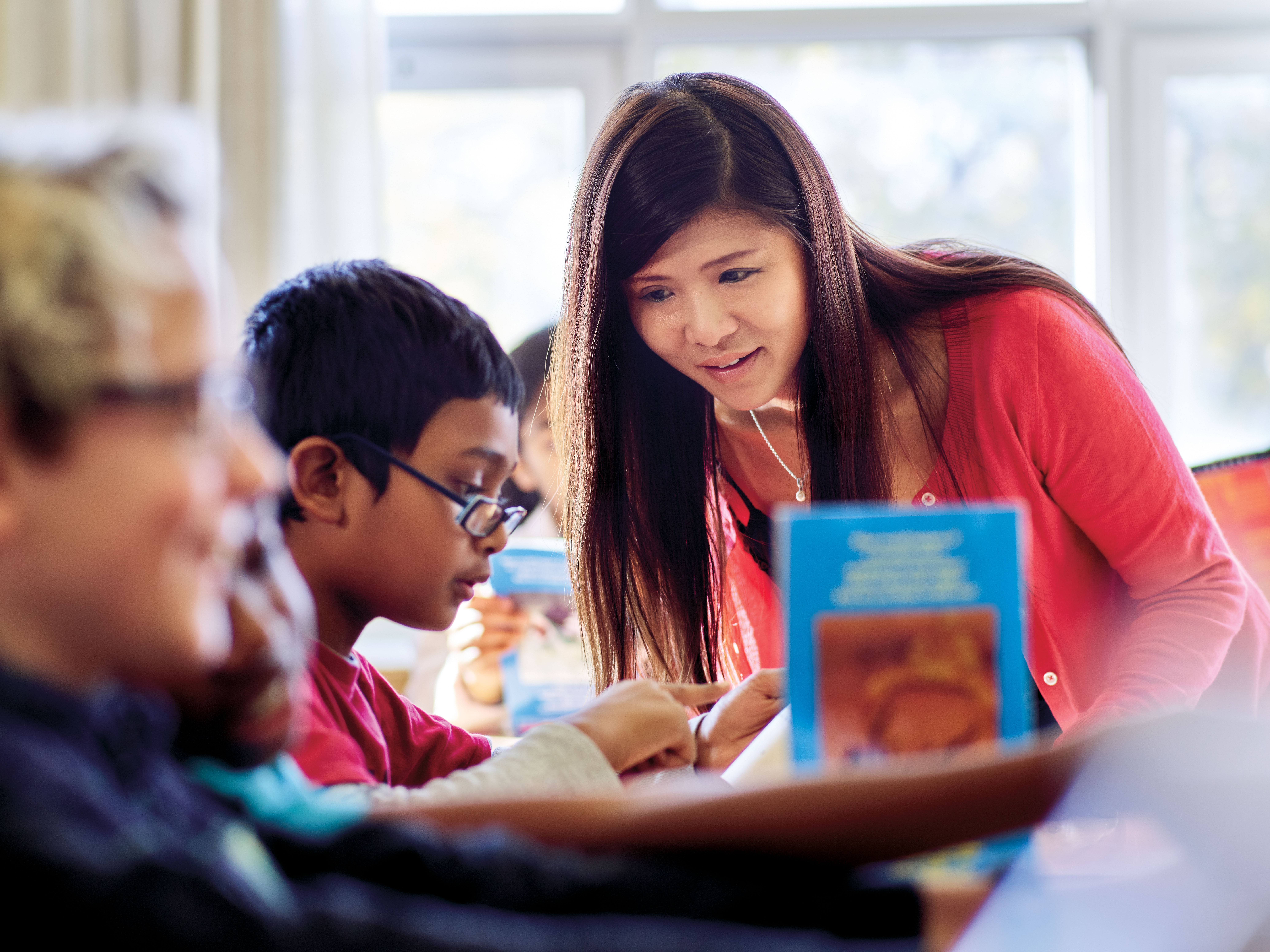 Photo of a teacher standing and leaning towards a seated student with glasses.