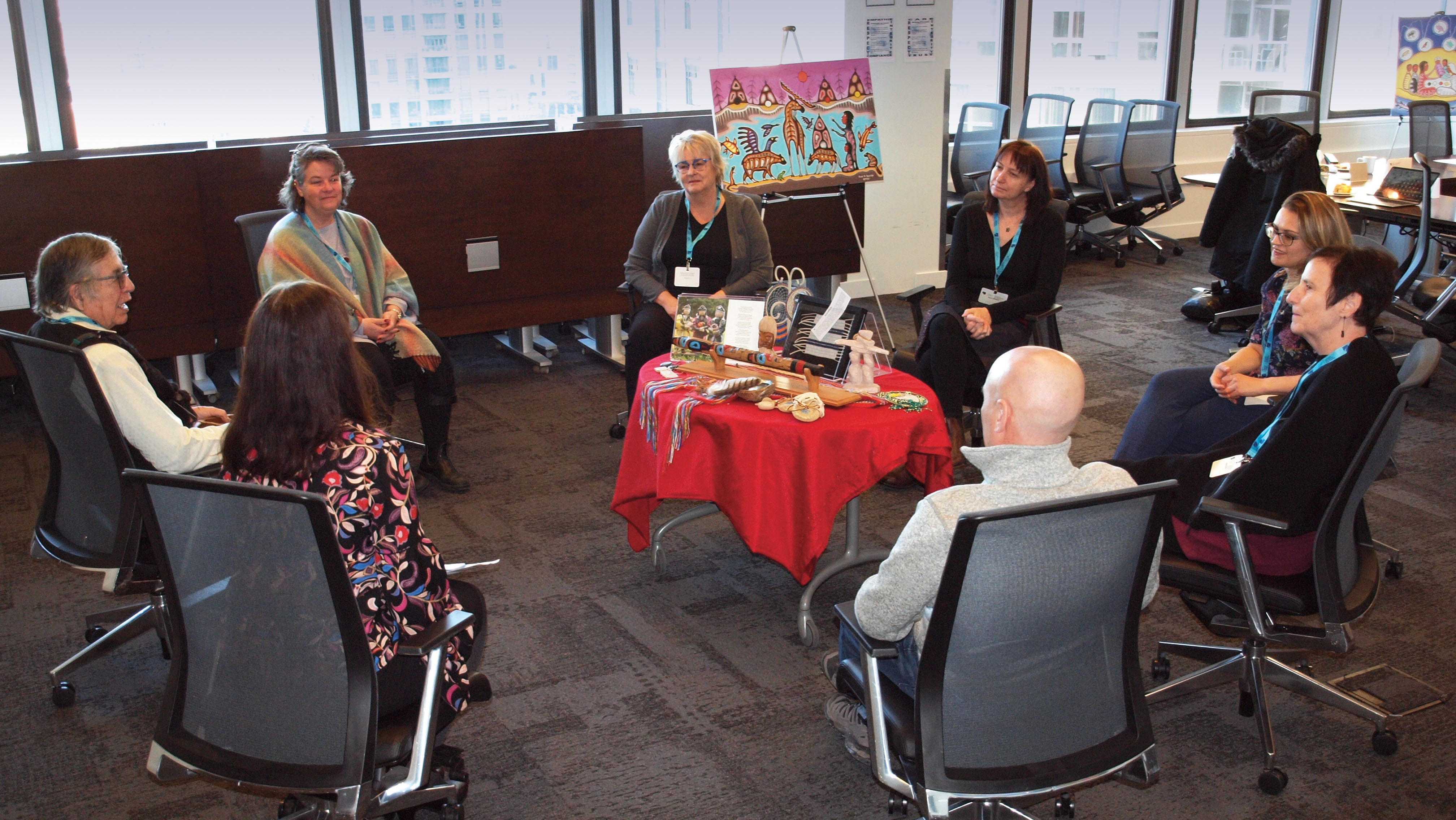 Photo of people sitting in chairs in a circle with a table in the middle.