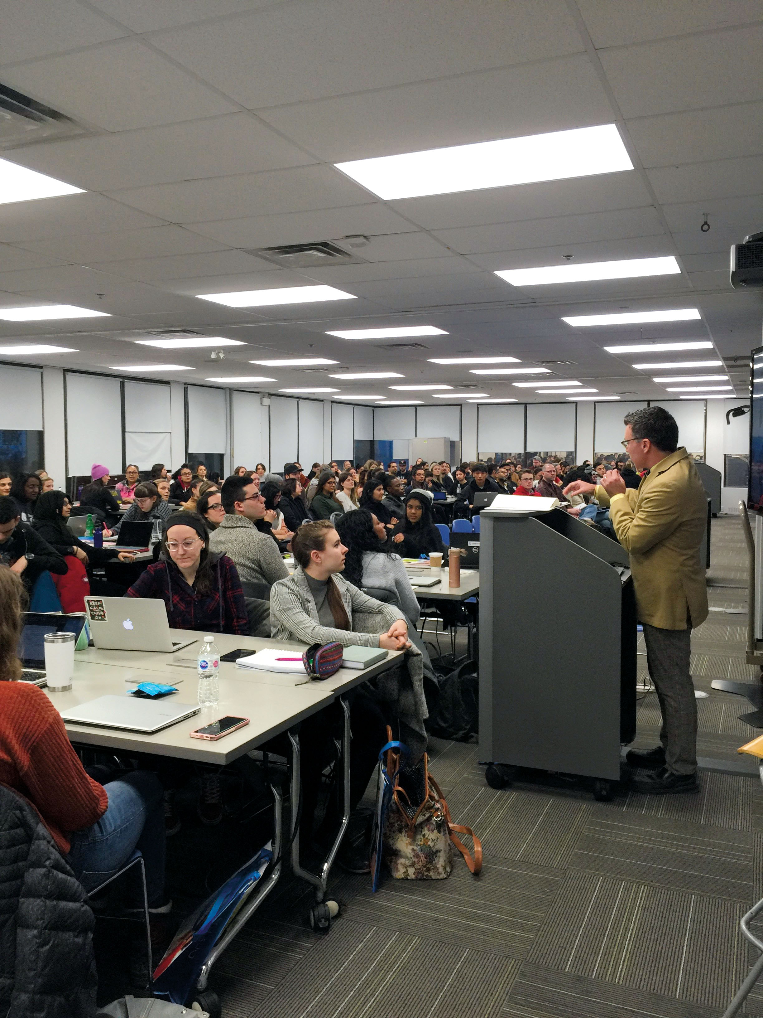 Photo of College Council Vice-Chair, Tim Gernstein, OCT, standing at a podium, speaking with a large group of students.